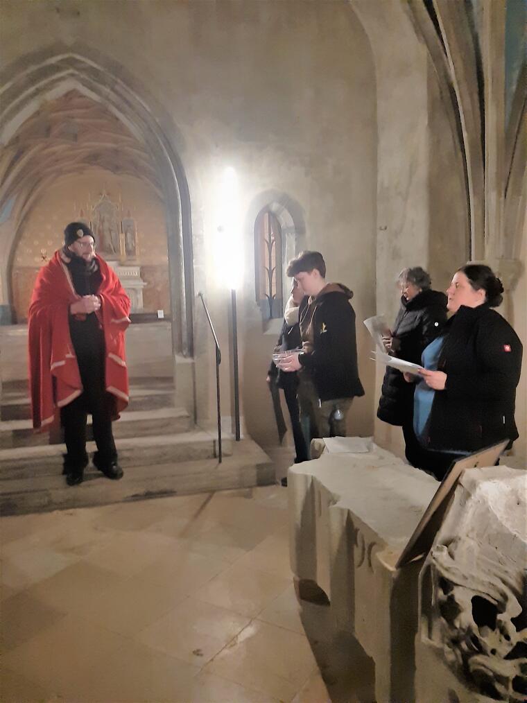 Fünf Personen in einer Kirche, eine davon trägt einen roten Mantel als Symbol für Pilatus. Die anderen haben Textzettel in den Händen.