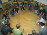 Jugendliche sitzen im Kreis und lösen eine Gemeinschaftsaufgabe: Einen Ball auf einen Holzturm setzen.