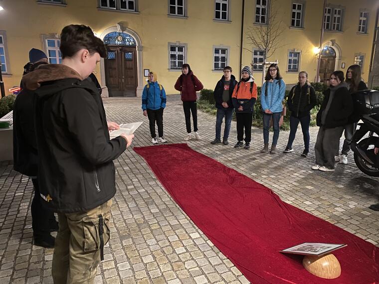 Junge Menschen stehen um eine rote Teppichbahn . Das ist die erste Station eines Kreuzweges.