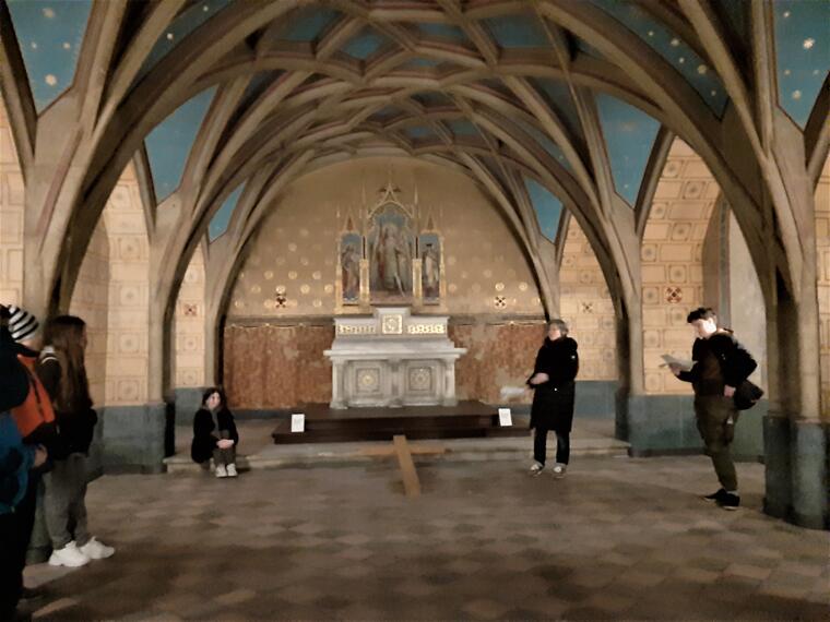Menschen sitzen und stehen in einer Kapelle. Vor dem Altar liegt ein großes Holzkreuz am Boden.