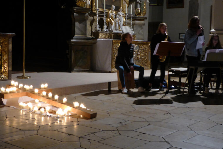 Holzkreuz am Boden liegend mit Kerzen, daneben eine Musikgruppe