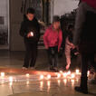 Personen stellen Kerzen an einem liegenden Holzkreuz in einer Kirche ab
