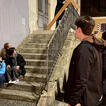 Jugendliche sitzen und stehen vor dem Treppenaufgang zu einer Kirche. Oben steht ein großes Holzkreuz.