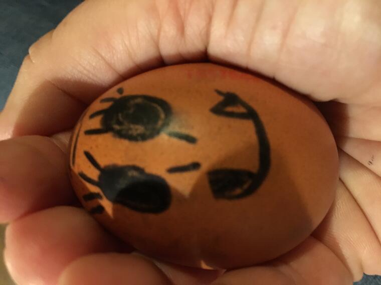 Ein mit einem Gesicht bemaltes Ei in einer Hand