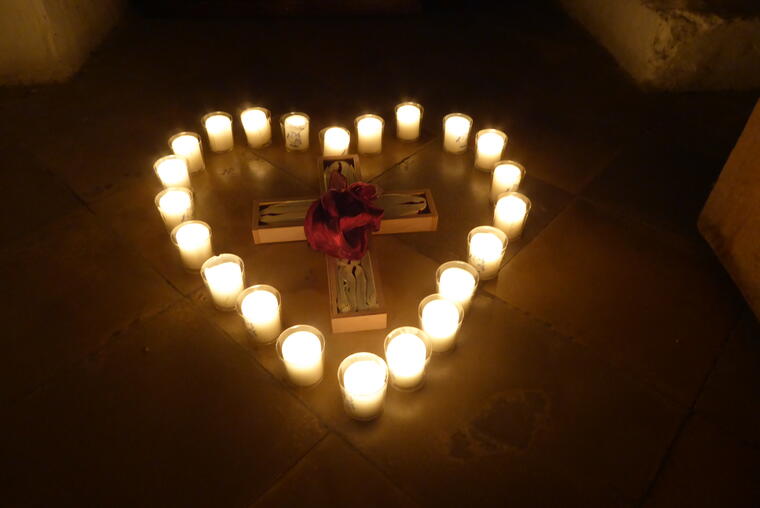 Ein Herz aus brennenden Teelichtern, in der Mitte ein Kreuz mit einem roten Tuch in der Mitte