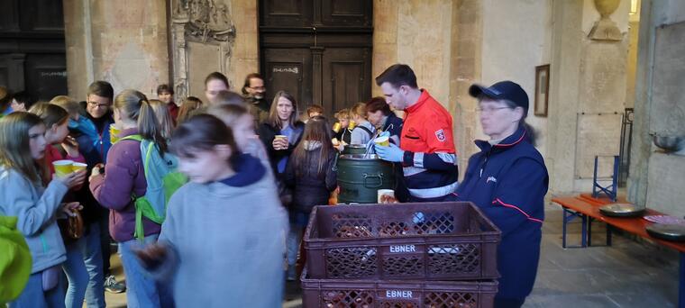 Jugendliche und Erwachsene werden von Ehrenamtlichen der Malteser mit Tee und Brezen verpflegt im Vorraum einer Basilika