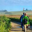 Menschen gehen durch Felder im Morgennebel mit einem Wallfahrtskreuz