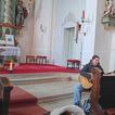 Drei Erwachsene an einem Altar, eine Frau spielt Guitarre