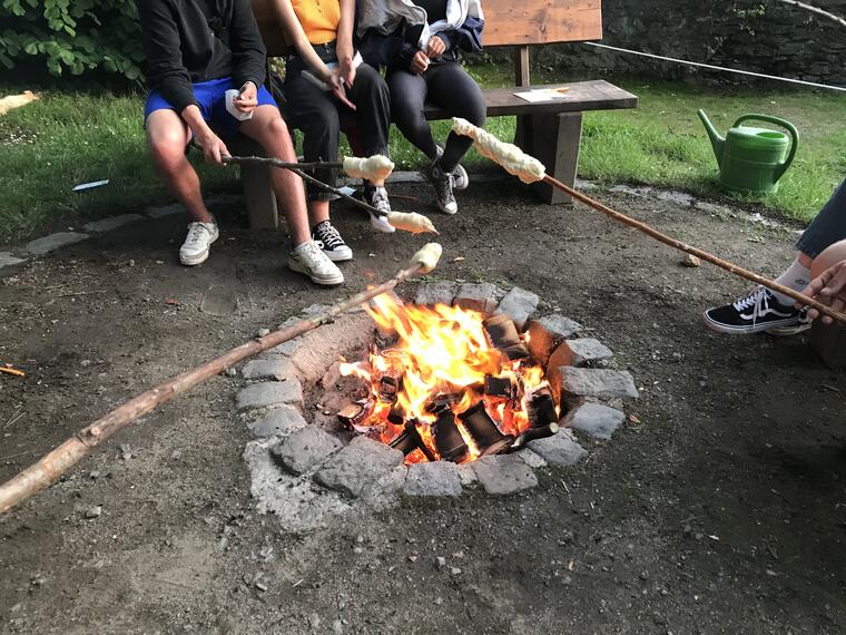 Jugendliche halten Stockbrot über ein Lagerfeuer