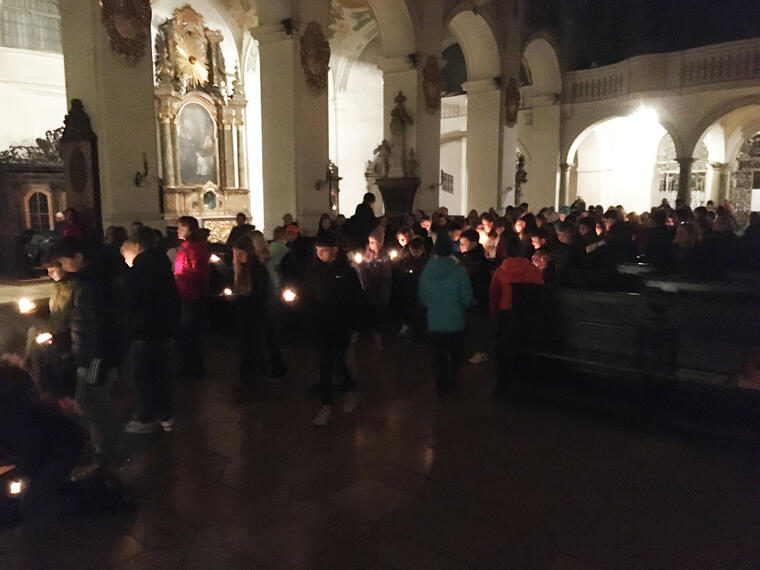 Kinder bringen Kerzen nach vorne zu einem Holzkreuz