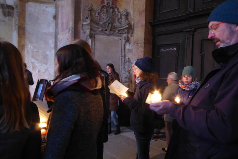 Menschen im Eingangsbereich einer Kirche mit Kerzen und Liebblättern in der Hand